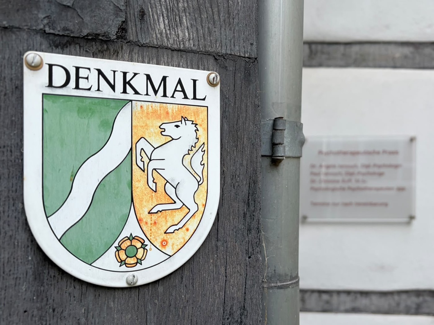Denkmalplakette mit dem Wappen des Landes Nordrhein-Westfalen am Fachwerkhaus, daneben unscharf das Praxisschild neben der Eingangstür.