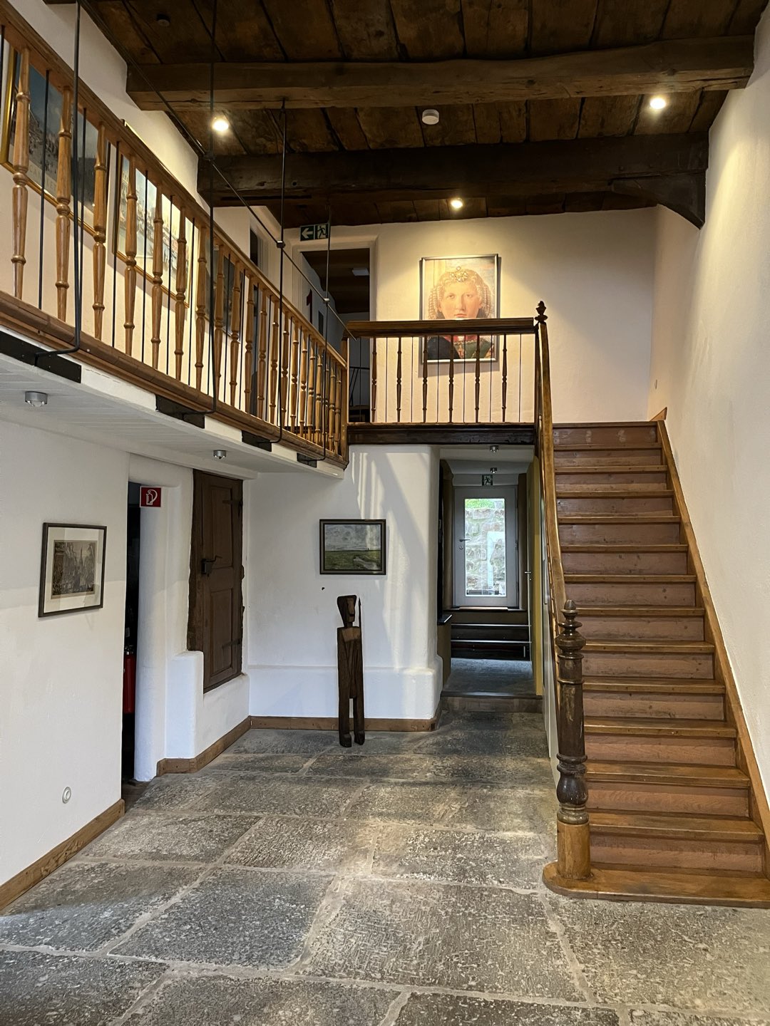 Zweigeschossiges Foyer der Praxis mit freiliegender Holzbalkendecke, Natursteinboden und offener Holztreppe im denkmalgeschützten Fachwerkhaus.