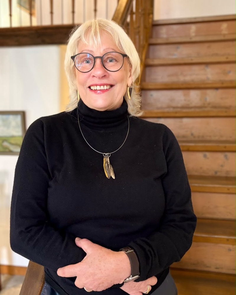 Portrait von Angela Janouch vor dem Treppengeländer der Praxis.