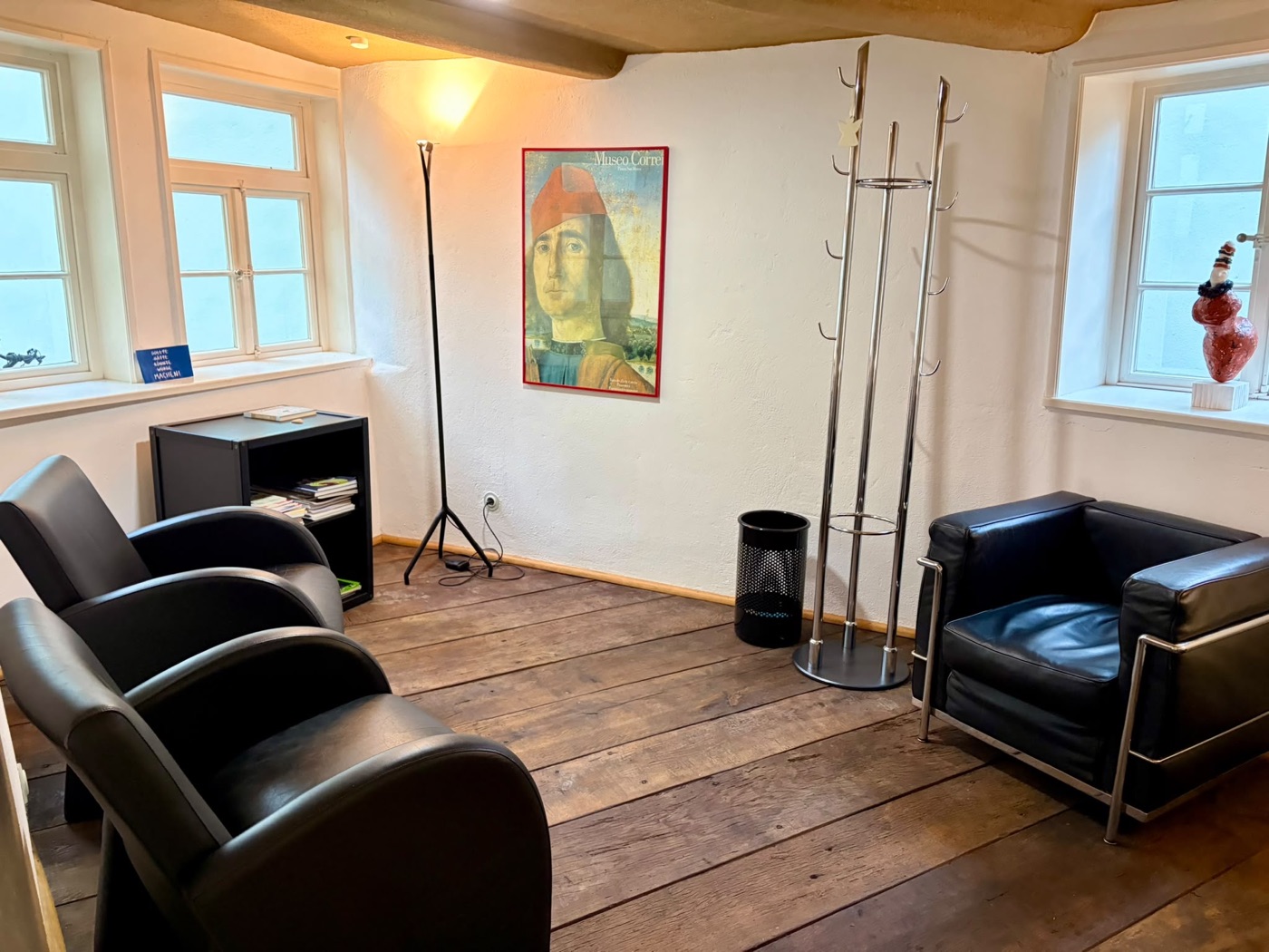 Warteraum mit Ledersesseln, Garderobe, Stehlampe und Kunstdruck an der weißen Wand.